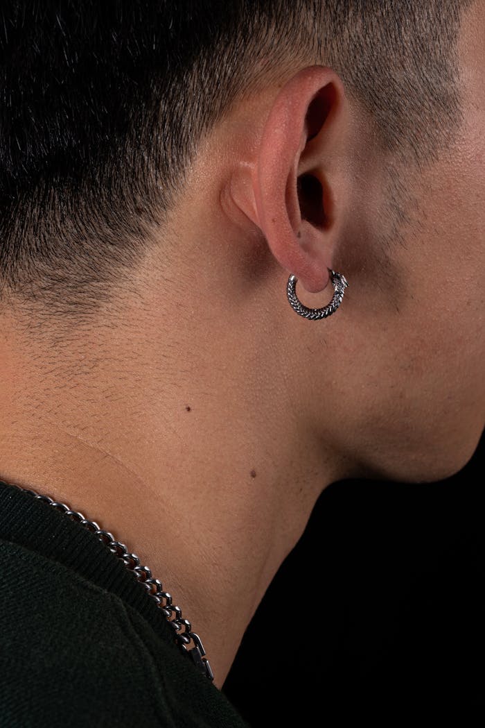 Close-up of a male ear wearing a silver snake-shaped earring. Modern and stylish.