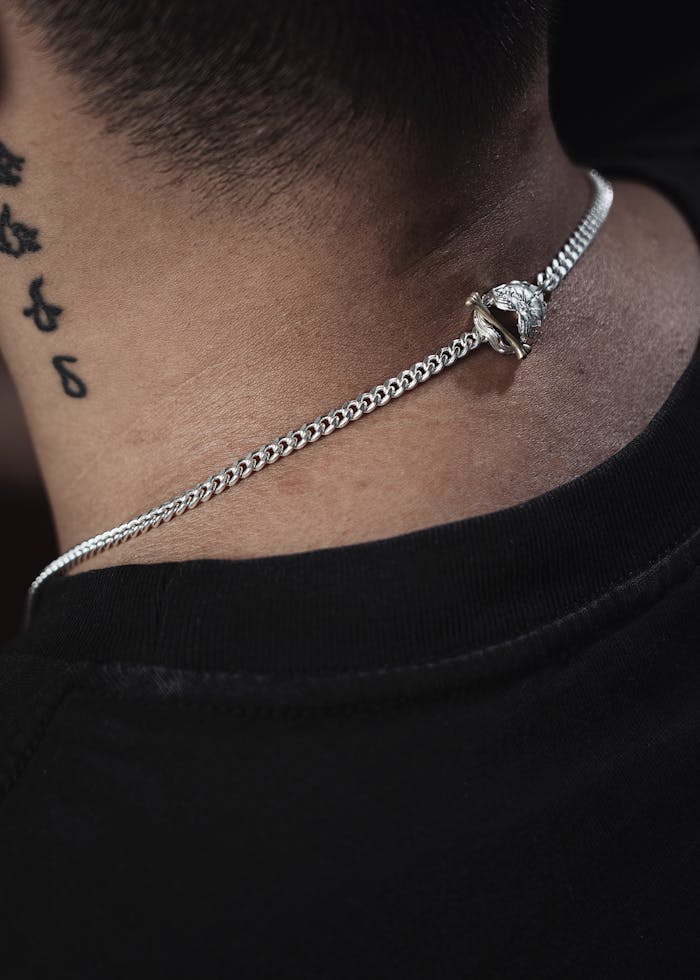 services-02 Close-up of a silver necklace on a male model's neck with tattoos.