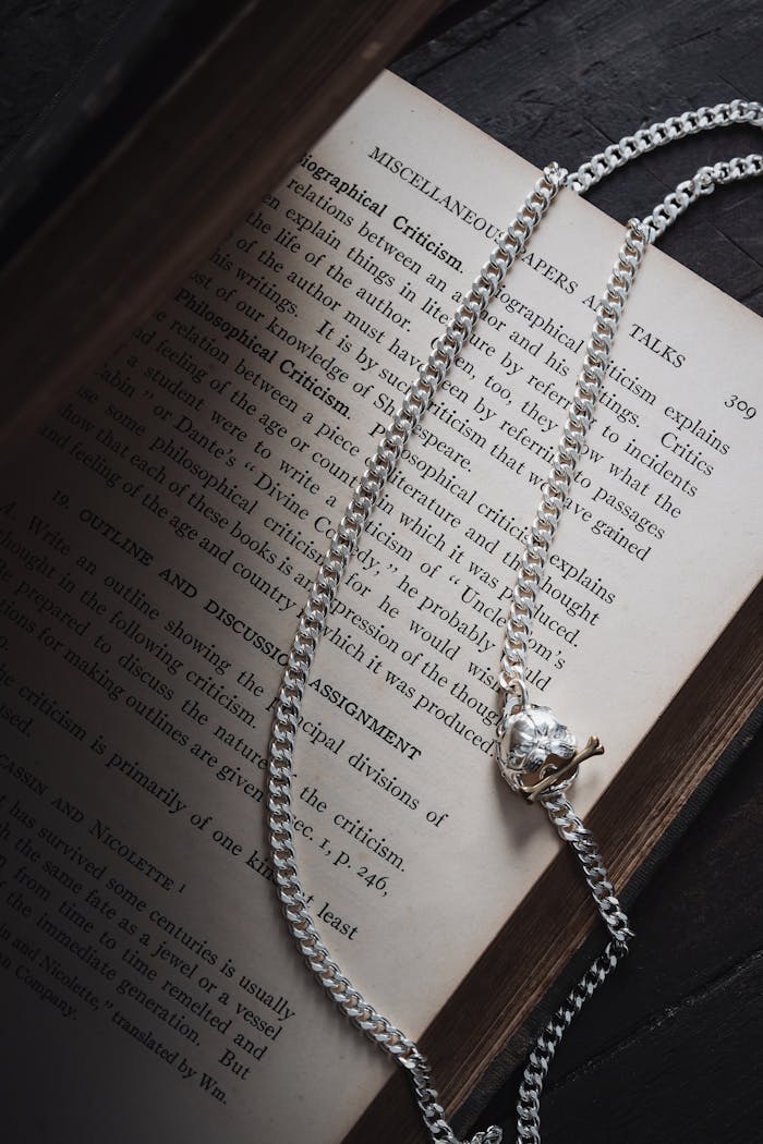 Artistic shot of a silver necklace draped over an open book, evoking elegance and mystery.