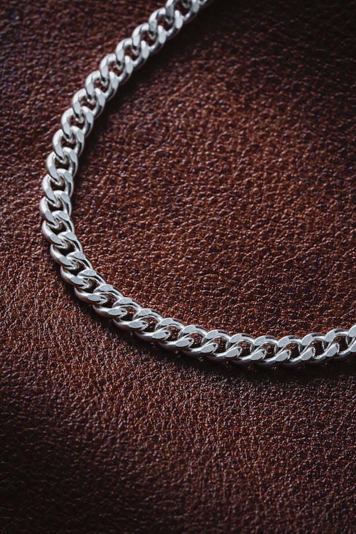 High-quality still life of a silver chain necklace displayed on textured brown leather. Ideal for fashion and jewelry concepts.