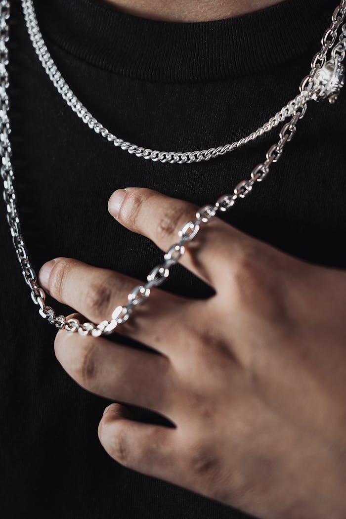 about-us-02 A detailed close-up of silver chains worn on a hand against a black t-shirt background, exuding style and elegance.