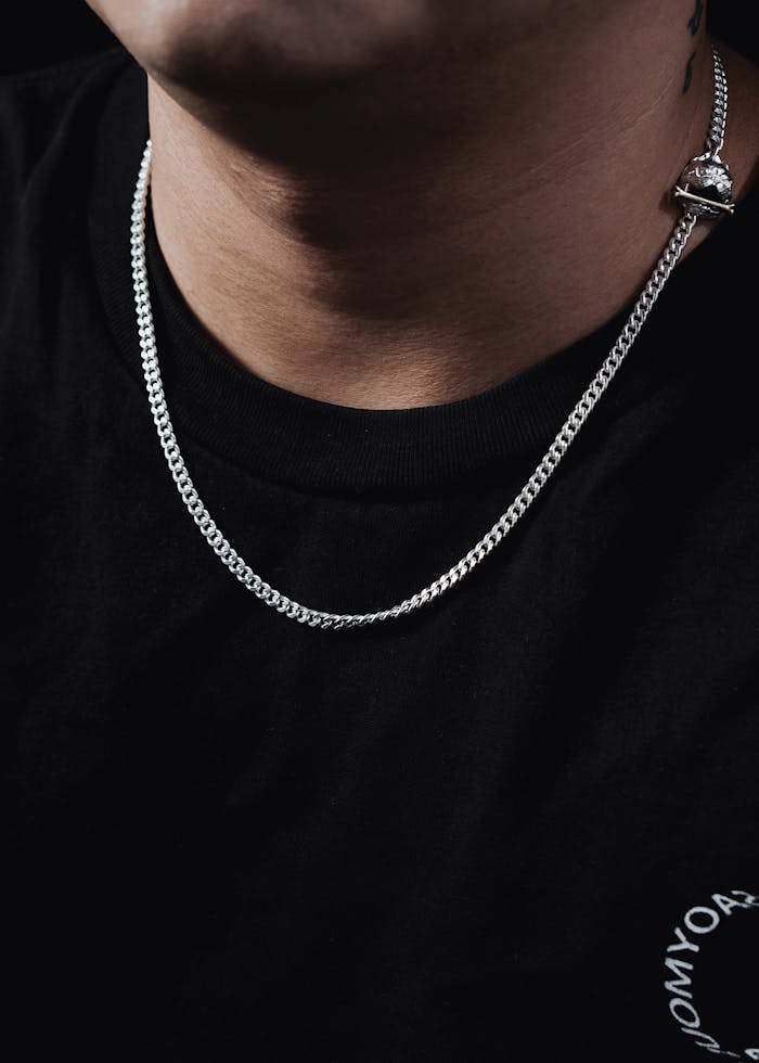 Close-up of a silver Cuban link chain necklace worn over a black t-shirt.