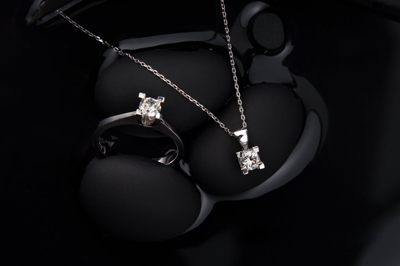 about-us-01 Luxurious silver diamond ring and pendant necklace on a black background, showcasing elegance and sophistication.